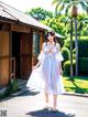 A woman in a white dress standing in front of a house.