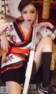 A woman in a kimono sitting on a chair holding a sword.