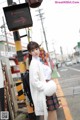 A woman in a white sweater and plaid skirt standing next to a traffic light.