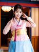 A woman in a pink and blue hanbok poses for a picture.