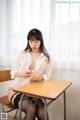 A woman sitting at a desk in a white shirt and black stockings.