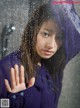 A woman in a purple raincoat standing in front of a window.