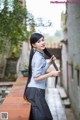 A woman with long black hair standing on a brick wall.